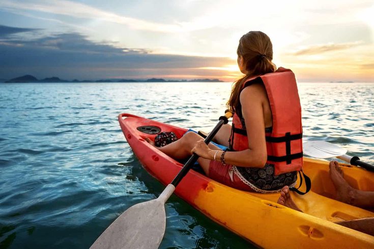 a man and woman in a kayak on the ocean at sunset or sunrise, back view