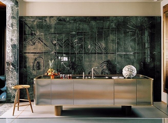 a kitchen with a metallic counter top and stools in front of an artistic wall