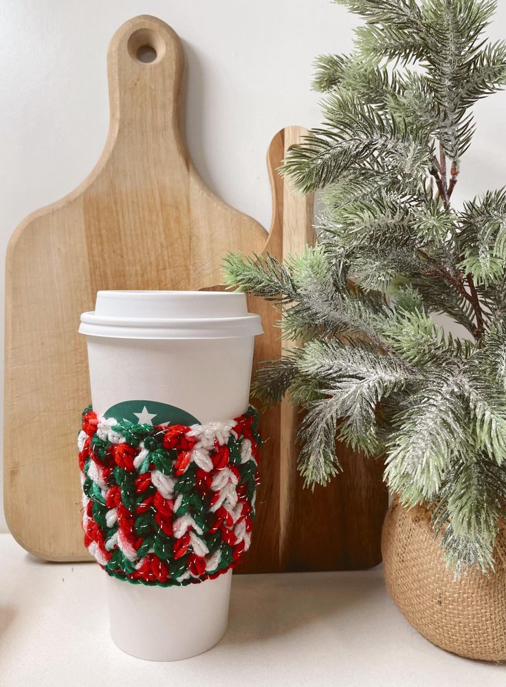 a coffee cup cozyie next to a potted pine tree and cutting board on a counter