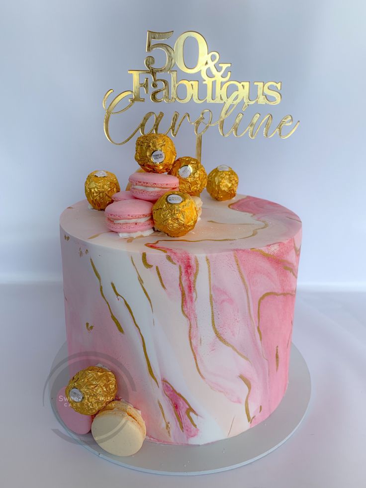 a pink marble cake with gold decorations on top and the number 50 is spelled out in cursive writing