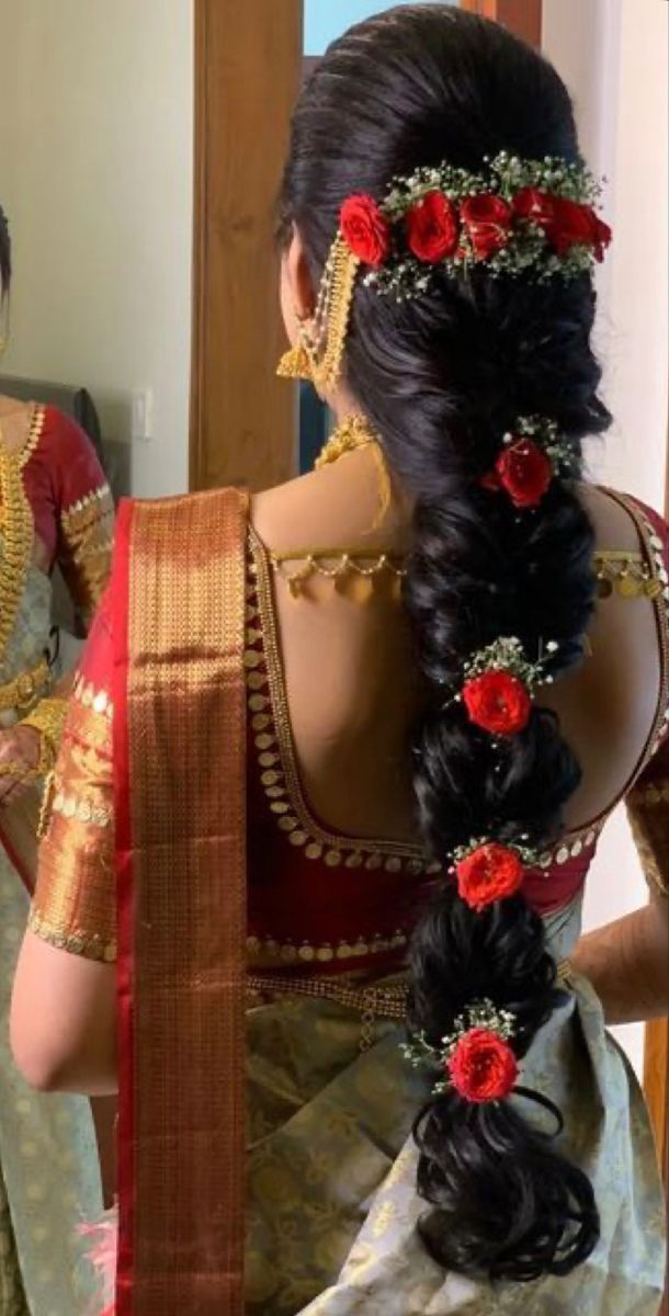 a woman in a red and gold sari with flowers on her hair is looking into the mirror