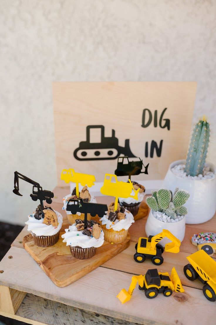 cupcakes are displayed on a wooden table with construction vehicles and cacti