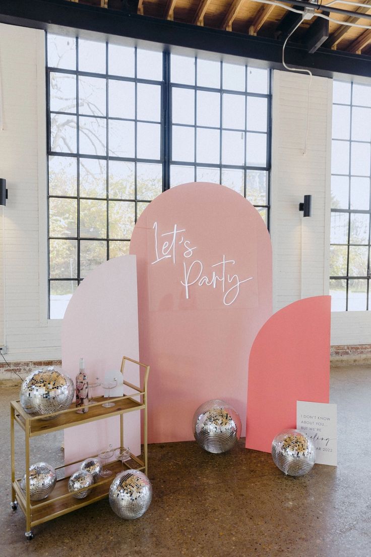 a pink and silver party decoration with balloons on the floor next to a sign that says let's party