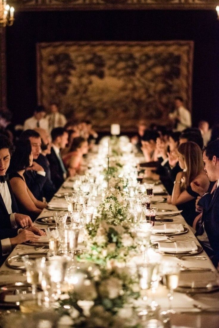 a long table with many people sitting at it and candles on the tables in front of them