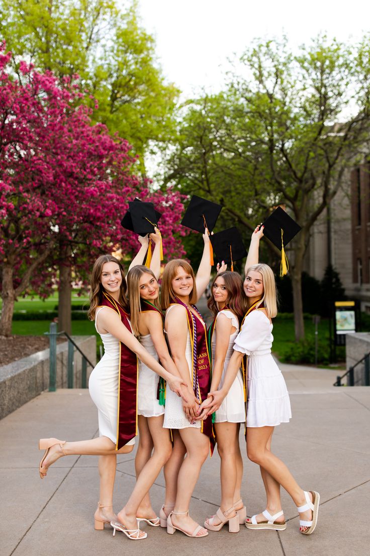 four young women in graduation gowns posing for the camera with their arms in the air