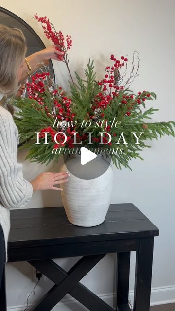 a woman arranging flowers in a white vase on a table with the words how to style holiday arrangements