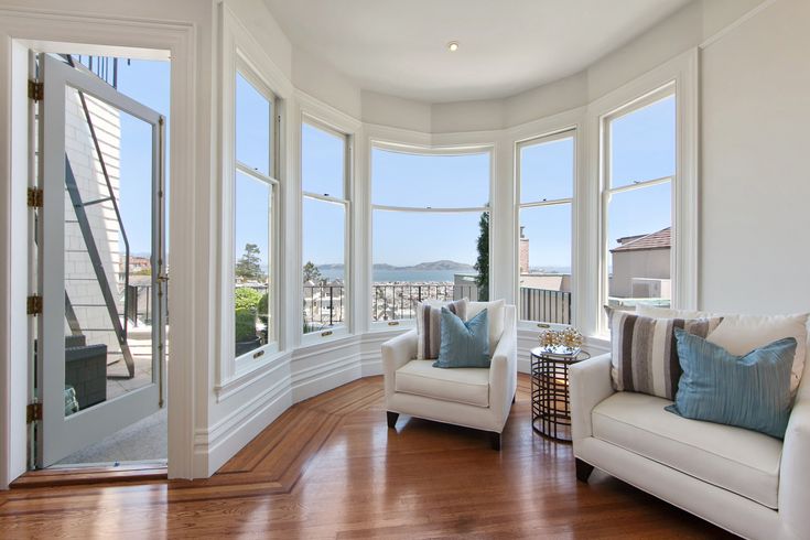 a living room filled with white furniture and large windows overlooking the ocean on a sunny day