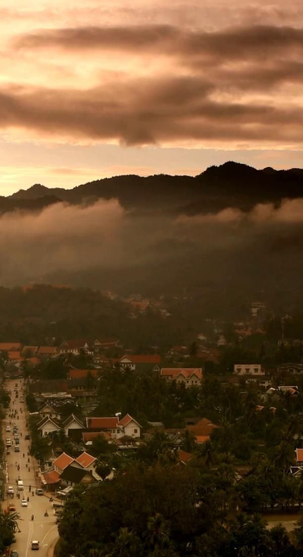 an aerial view of a town with mountains in the background and clouds hovering over it