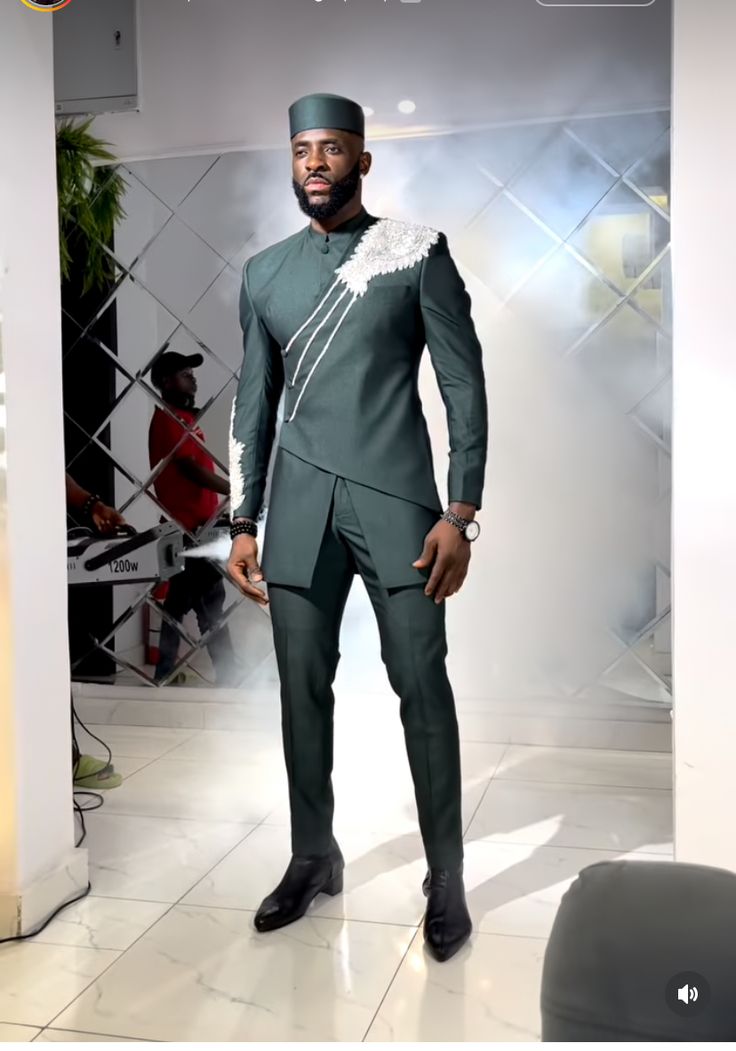 a man in a green suit and hat standing next to a white wall with a mirror behind him