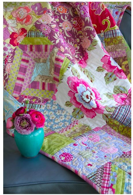 a blue vase filled with pink flowers on top of a couch next to a blanket