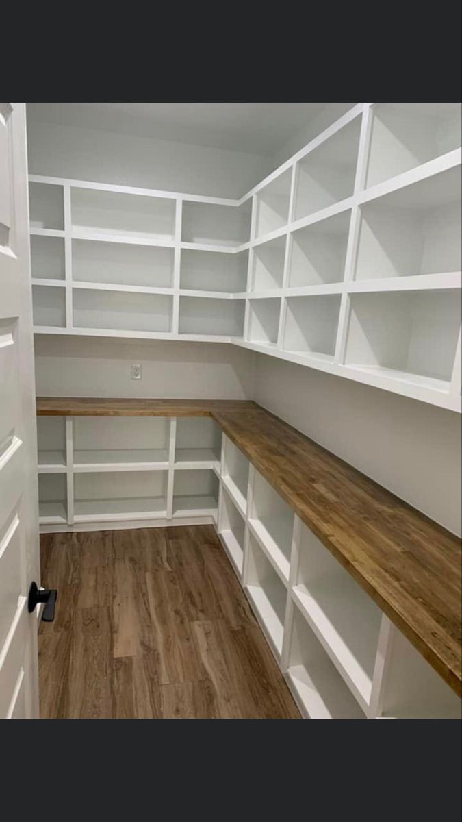 an empty walk in closet with white shelving and wood flooring