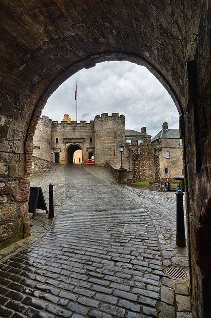 an archway leading into a castle like area with cobblestone floors and stone walls