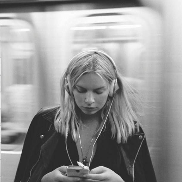 a woman with headphones is looking at her cell phone while riding the subway train