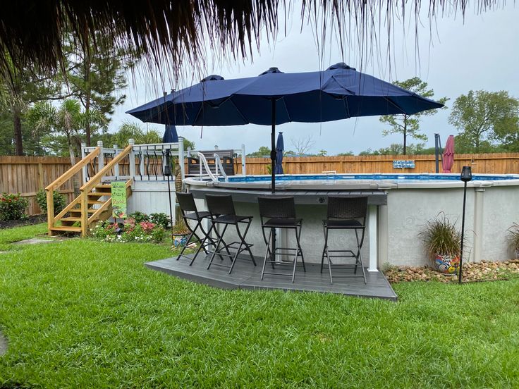 an outdoor pool with chairs and umbrellas in the grass next to a wooden deck