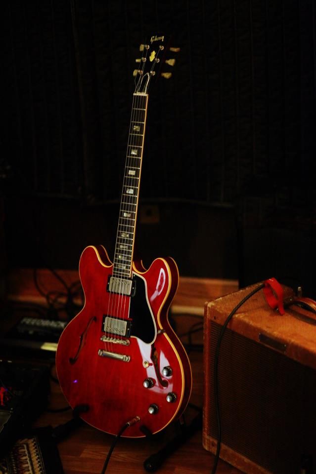 a red electric guitar sitting on top of a wooden floor next to a suitcase and amp