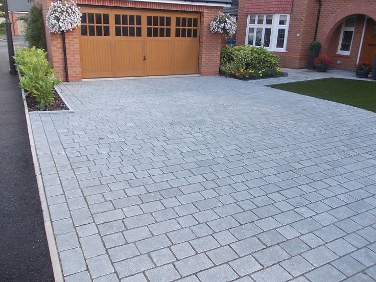 a large brick driveway in front of a house with two garage doors on each side