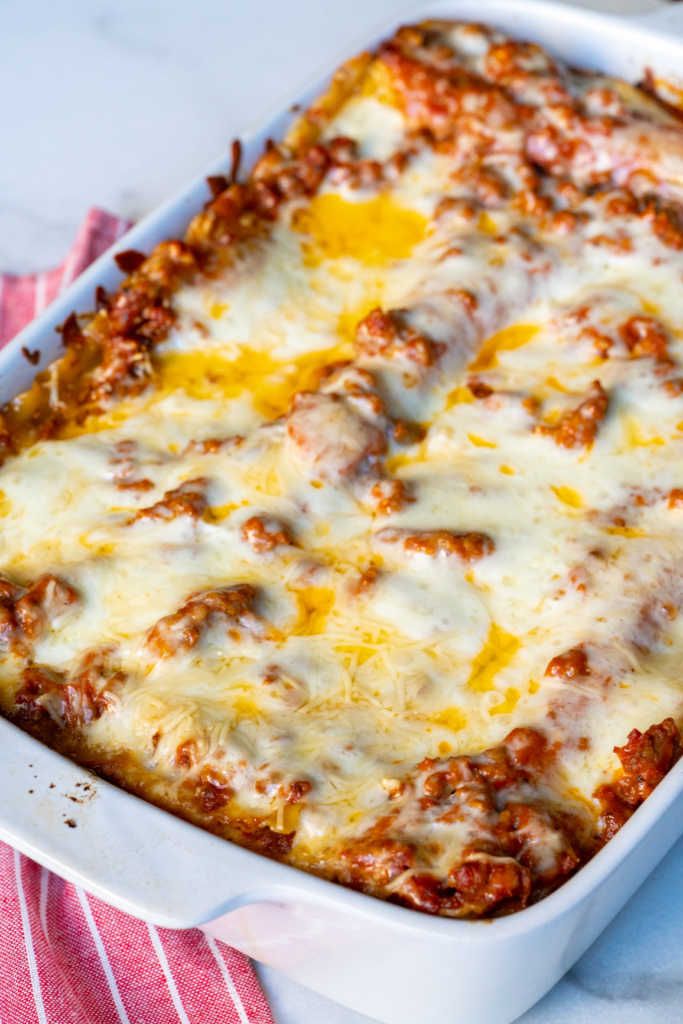 a casserole dish with cheese and meat in it on a red and white towel