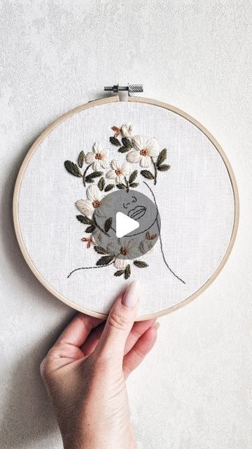 someone is holding up an embroidery project with flowers and a video player in the middle