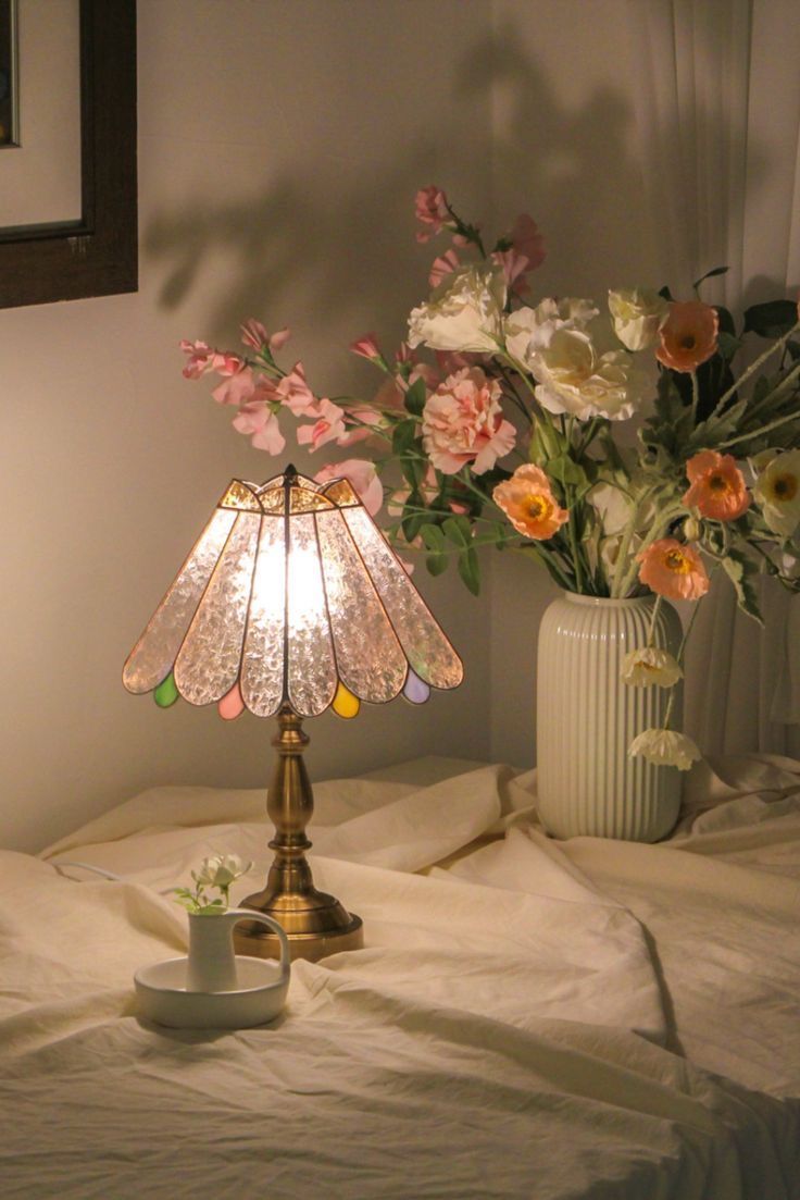 a lamp that is on top of a bed with flowers in the corner next to it