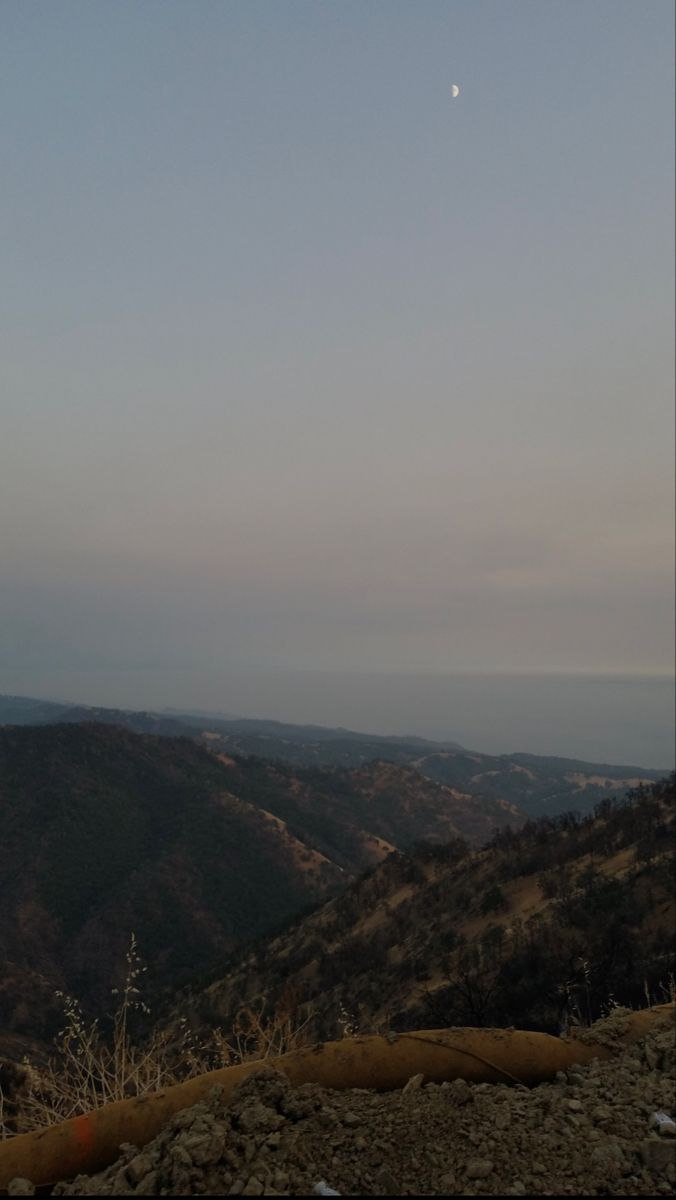 the moon is setting over the mountains in the distance, and there are no clouds