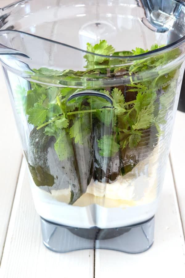 a blender filled with green vegetables on top of a white table