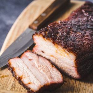 sliced pork on a cutting board with knife and fork next to it, ready to be eaten