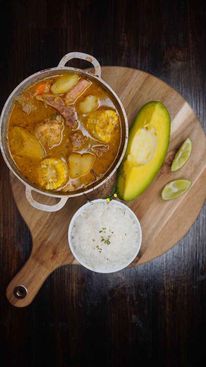 a wooden cutting board topped with a bowl of soup next to an avocado