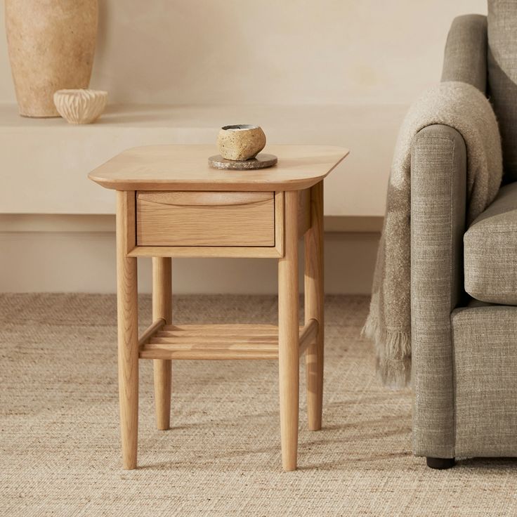 a small wooden table sitting next to a couch in a living room with a vase on it