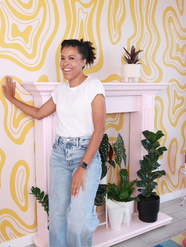 a woman standing in front of a pink fireplace with potted plants on top of it