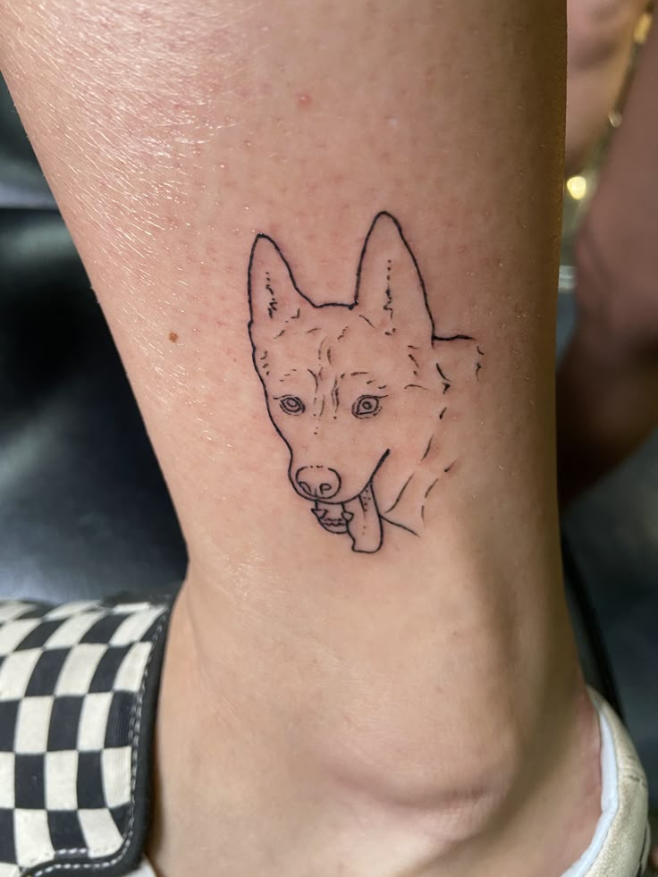 a small tattoo on the ankle of a woman with a dog's face drawn on it