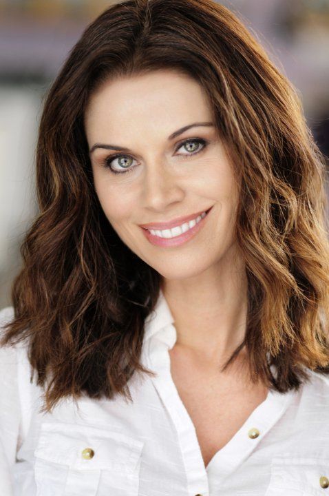 a woman with long brown hair and blue eyes smiles at the camera while wearing a white shirt