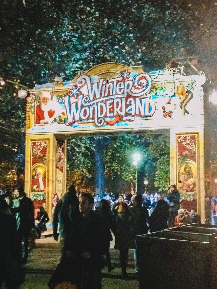 the entrance to winter wonderland at night with people walking under it and trees in the background