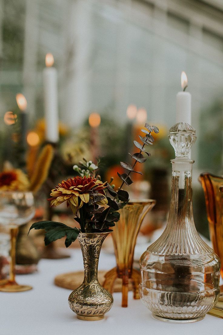 an assortment of glass vases and candles on a white table cloth with flowers in them