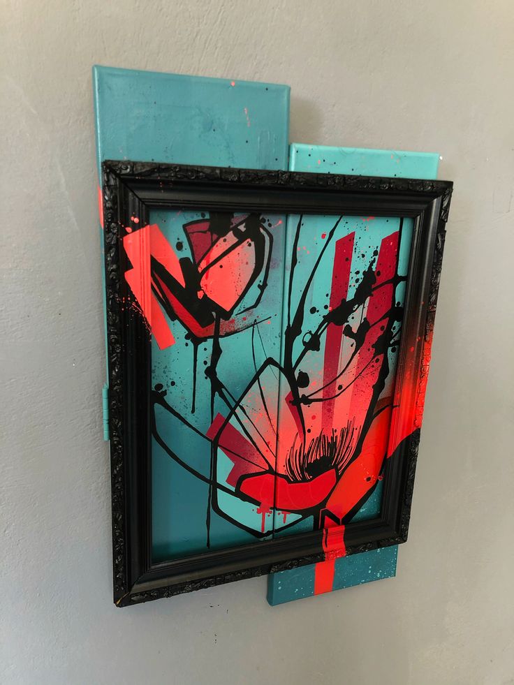 a painting is hanging on the wall next to a blue frame with red flowers painted on it