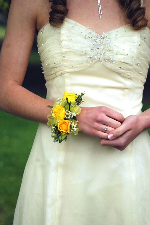 a woman in a white dress with yellow flowers on her wrist and wedding band around her arm