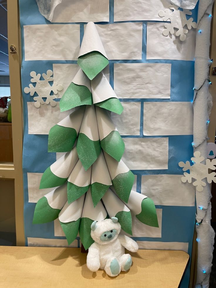 a paper christmas tree sitting on top of a table next to a teddy bear and snowflakes