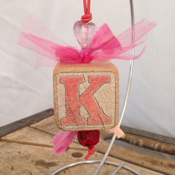 an ornament with the letter k on it hanging from a wire and pink ribbon