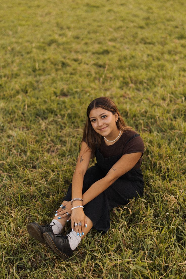 a woman sitting in the grass with her legs crossed and one hand on her knee