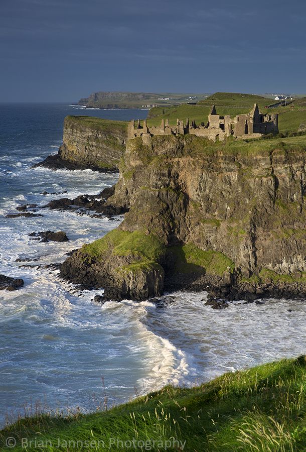 an old castle sits on the edge of a cliff overlooking the ocean with waves crashing against it