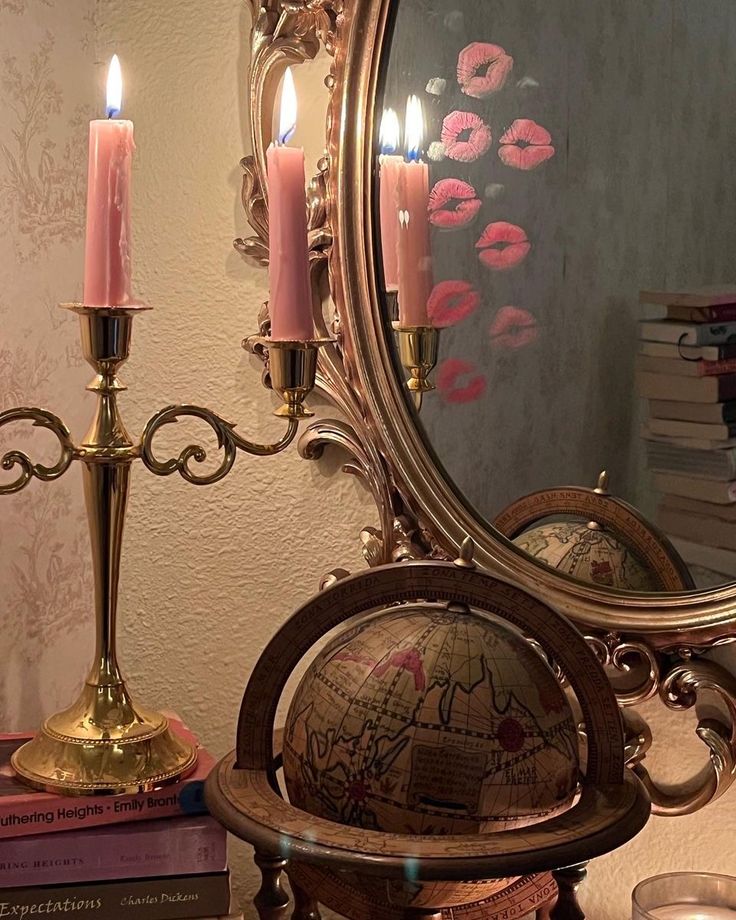 a globe and two candles on a table in front of a mirror with pink flowers