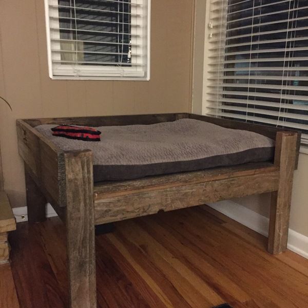 a dog bed sitting on top of a wooden floor next to a window with blinds