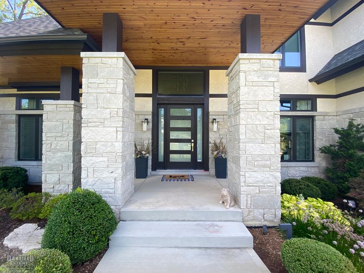 the front entrance to a modern home with stone pillars and wood shinning on the roof