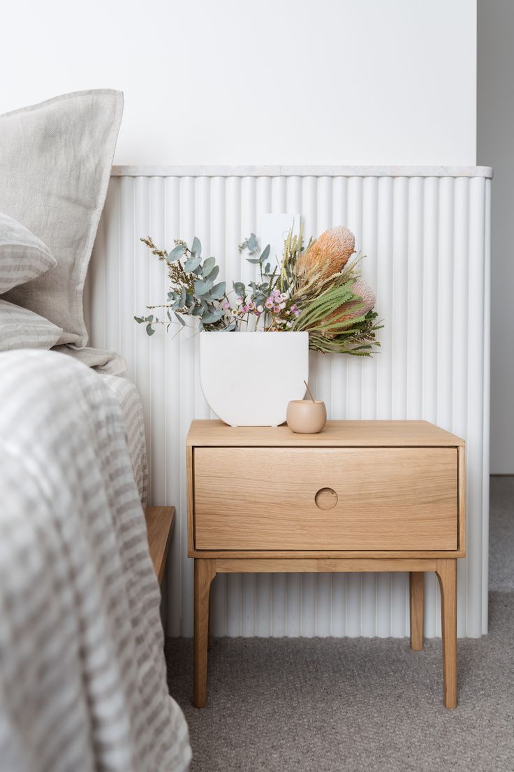 a nightstand with flowers on it next to a bed