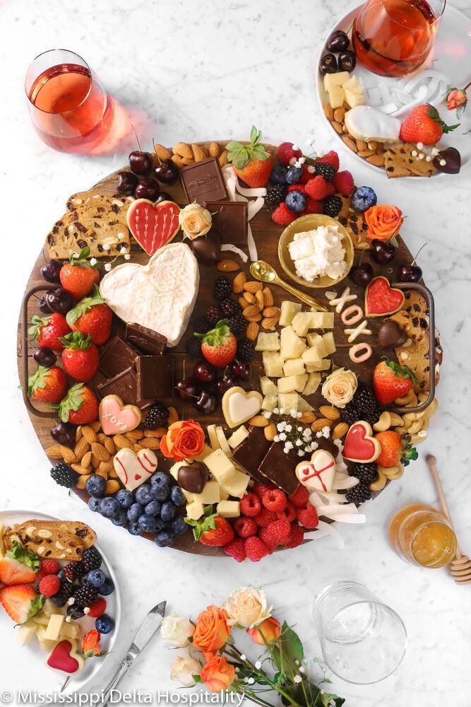 chocolate and cheese dessert board on a marble table with fruit, nuts, crackers, and wine glasses