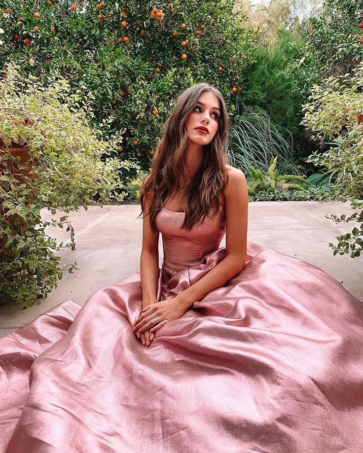 a woman in a pink dress sitting on the ground with an orange tree behind her