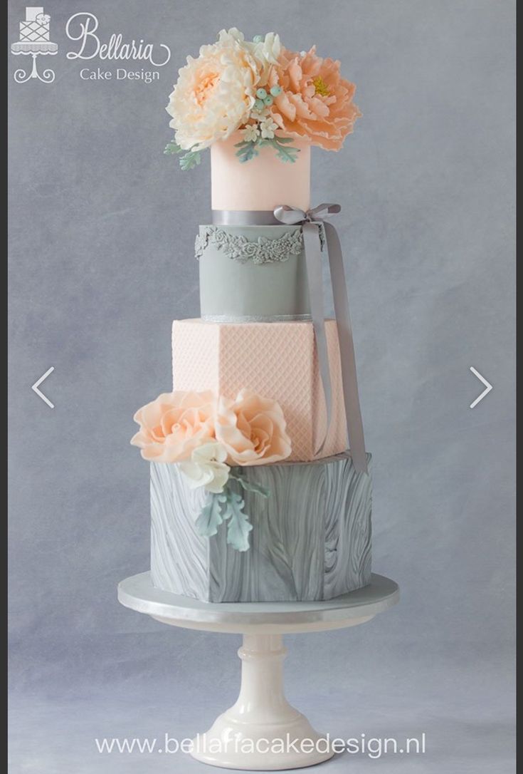 a three tiered cake decorated with flowers and ribbons on a white pedestal in front of a gray background