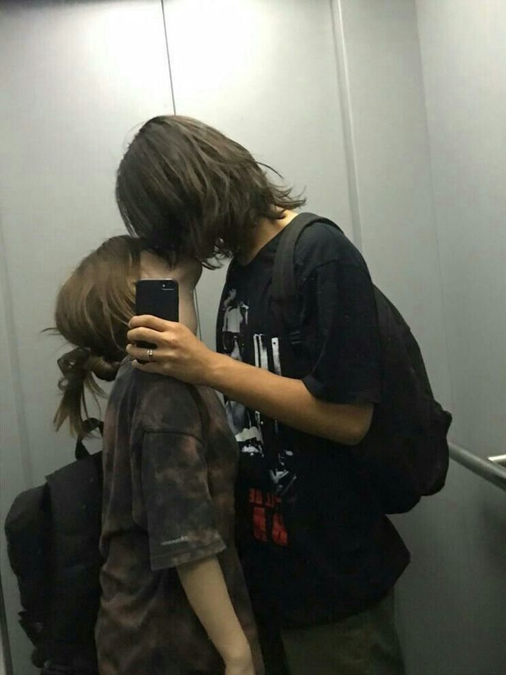 a boy and girl standing in front of a mirror looking at their cell phones together