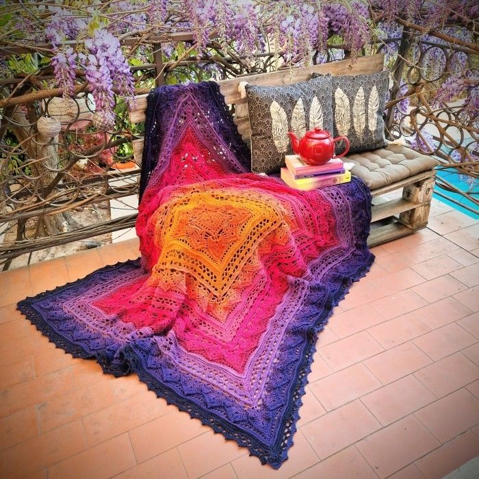 a crocheted blanket sitting on top of a wooden bench next to a potted plant