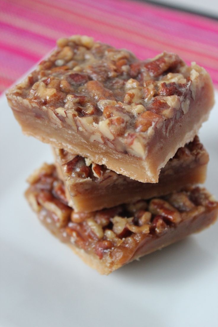 three pieces of pecan bar sitting on top of a white plate next to a pink striped table cloth