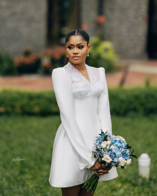 a woman in a short white dress holding a blue and white bouquet with her hands on her hips